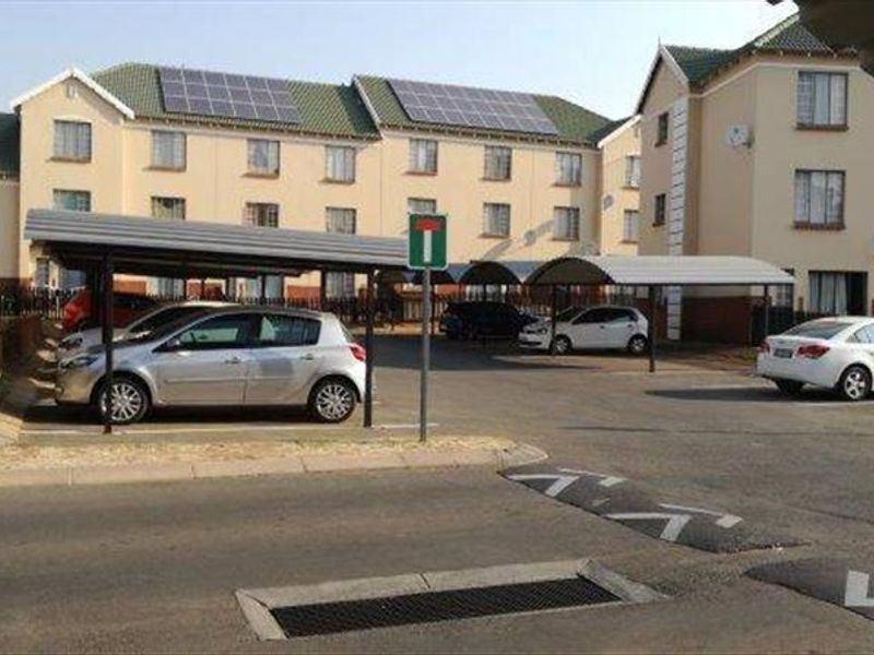 Exterior view of the apartment complex featuring covered parking bays, paved driveway, and solar panels installed on the roof.