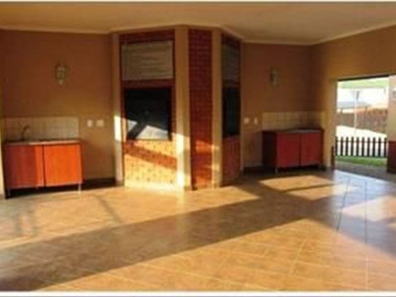 Spacious covered patio featuring a built-in braai, tiled flooring, and integrated cabinetry with a sink, ideal for outdoor entertaining.