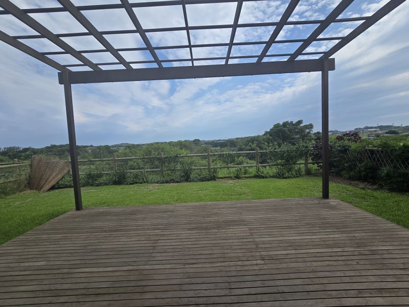 Outdoor timber deck featuring a pergola structure, overlooking a garden area with rural views and perimeter fencing.
