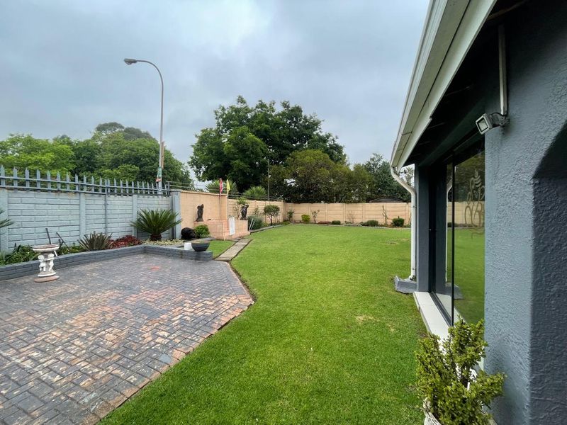 A well-maintained rear garden featuring a paved patio area, a spacious lawn, and secure perimeter walling, accessible via sliding glass doors.