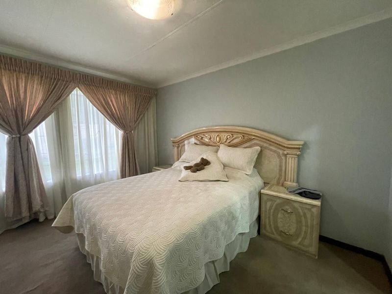 A standard bedroom featuring carpeted flooring, neutral wall paint, and large windows with installed curtain rails.