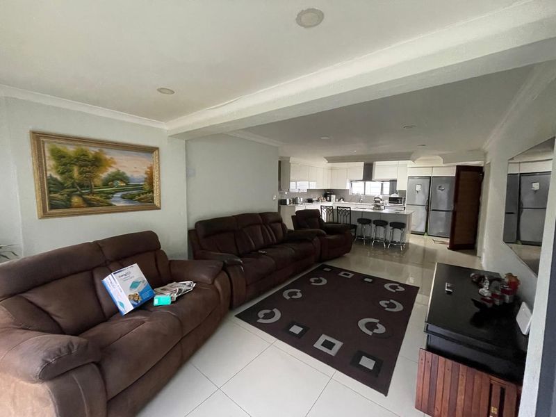 Spacious open-plan living area featuring a modern kitchen with a central island, recessed lighting, and neutral tiled flooring throughout.