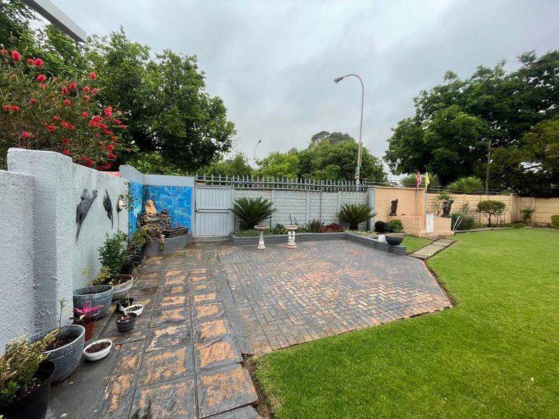 A rear garden featuring a paved patio area, established lawn, and perimeter boundary walls with integrated water features.