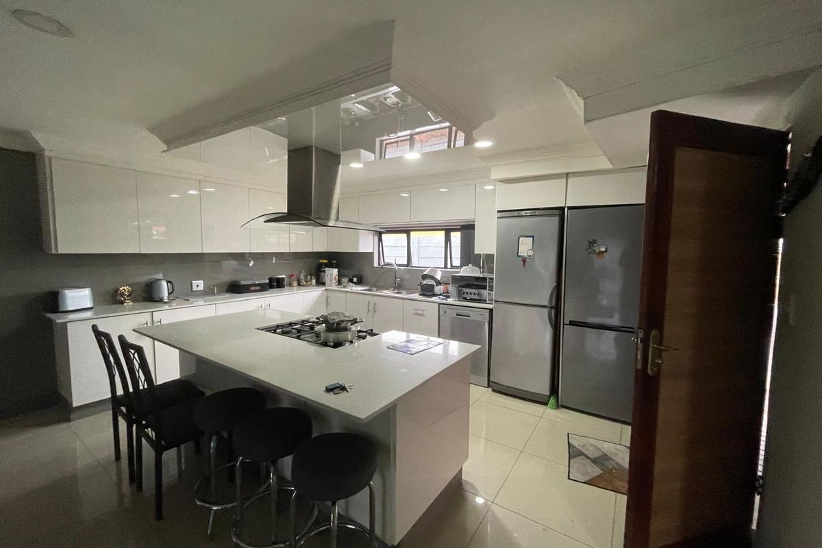 Modern kitchen featuring a central island with a built-in hob, sleek gloss cabinetry, integrated appliances, and tiled flooring.