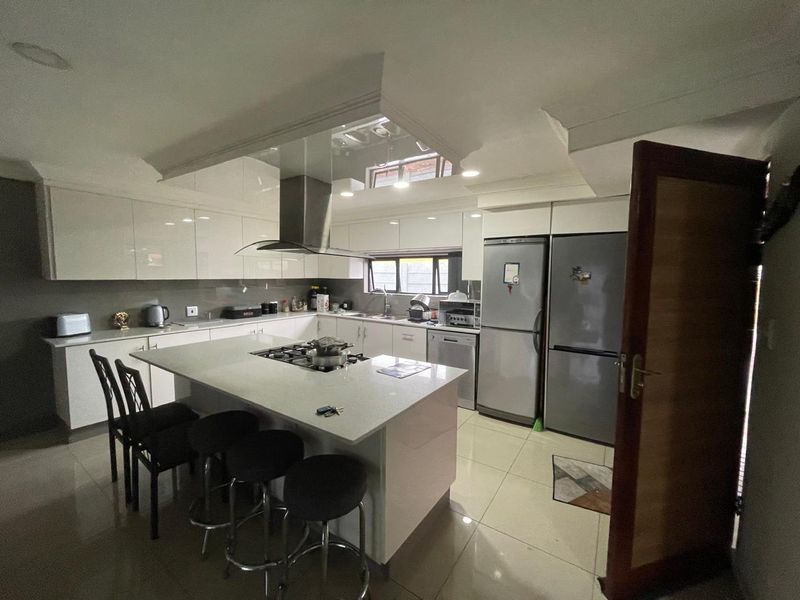 Modern kitchen featuring a central island with a built-in hob, sleek gloss cabinetry, integrated appliances, and tiled flooring.