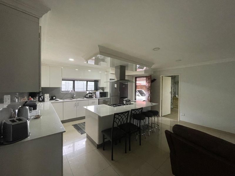 Modern kitchen featuring a central island with a gas hob, sleek white cabinetry, quartz countertops, and polished tile flooring.
