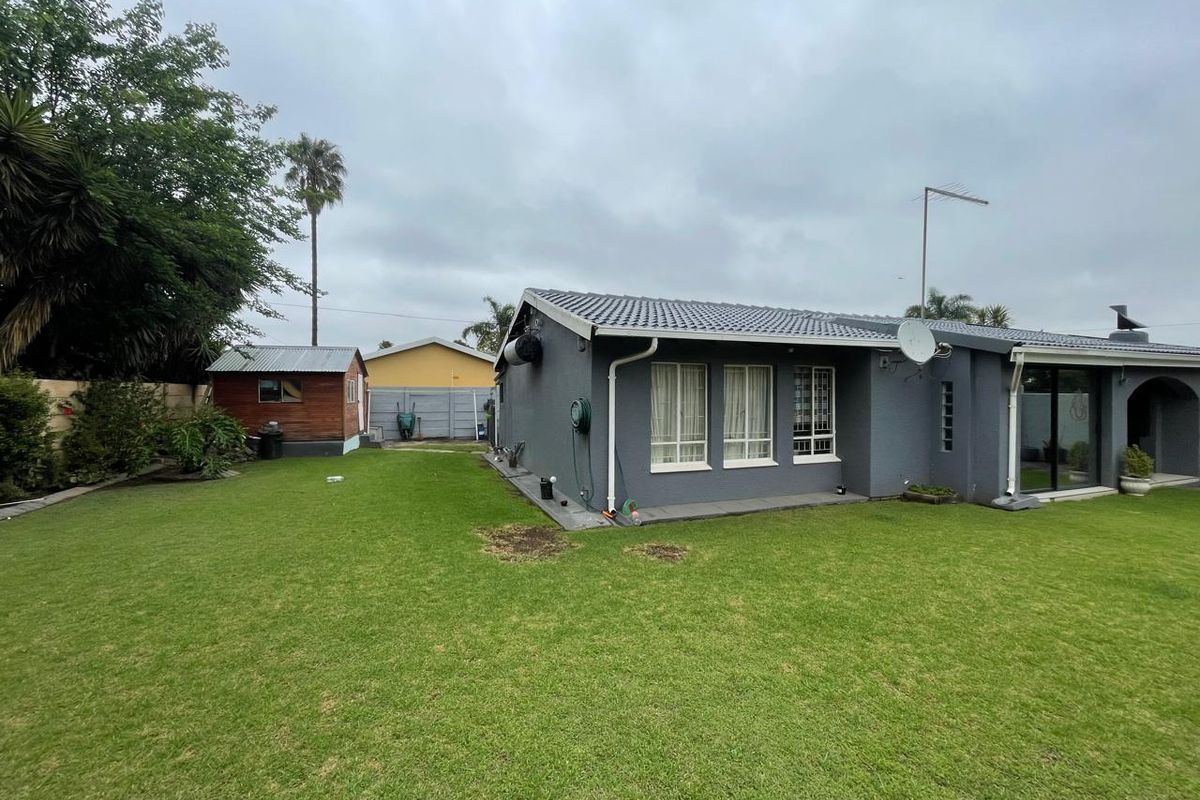 Rear view of the property featuring a grey rendered facade, tiled roof, sliding glass doors, and a spacious garden with a detached storage shed.