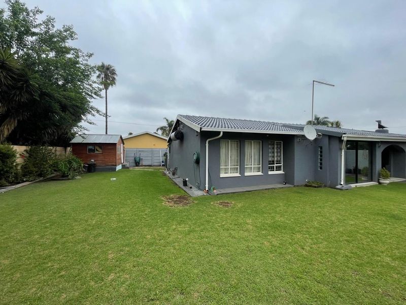 Rear view of the property featuring a grey rendered facade, tiled roof, sliding glass doors, and a spacious garden with a detached storage shed.