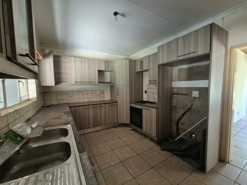 A dated kitchen featuring built-in cabinetry, a double bowl sink, and a built-in oven, currently requiring significant repairs and cosmetic updates.