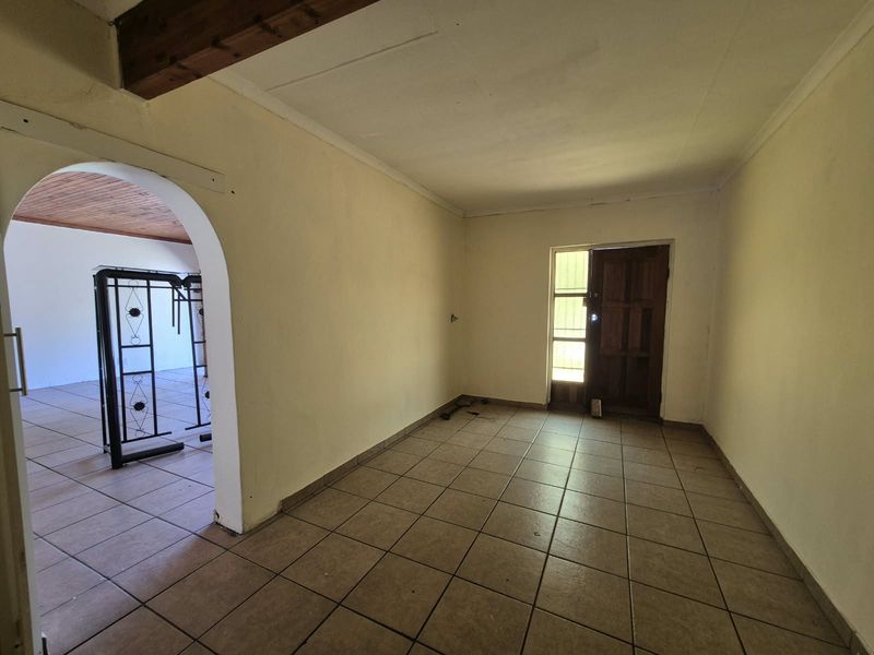 An empty entrance hall featuring tiled flooring, an arched transition to the adjacent room, and a traditional timber front door with exposed ceiling beams.