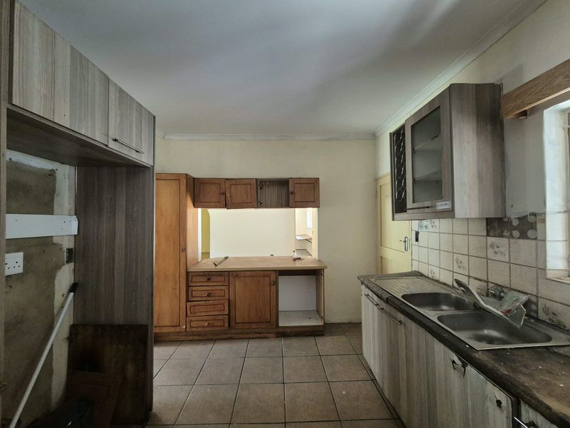A dated kitchen space featuring a double bowl sink, tiled backsplash, and a mix of wood-finish cabinetry, currently in need of renovation.