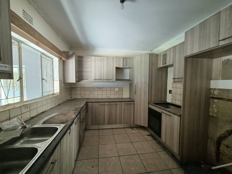A functional kitchen featuring built-in cabinetry, a double basin sink, and tiled finishes, currently vacant and requiring cosmetic updates to modernize the space.