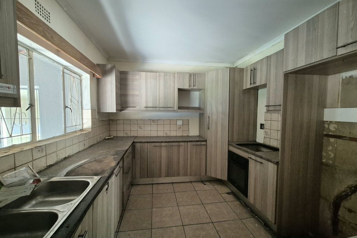 A functional kitchen featuring built-in cabinetry, a double basin sink, and tiled finishes, currently vacant and requiring cosmetic updates to modernize the space.