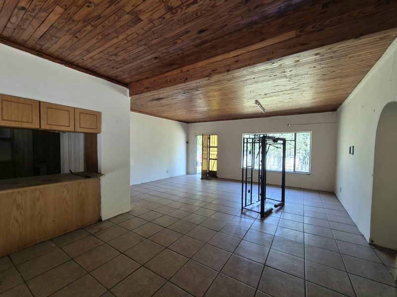 Spacious open-plan living area featuring a timber tongue and groove ceiling, ceramic floor tiles, and a built-in kitchen serving counter.