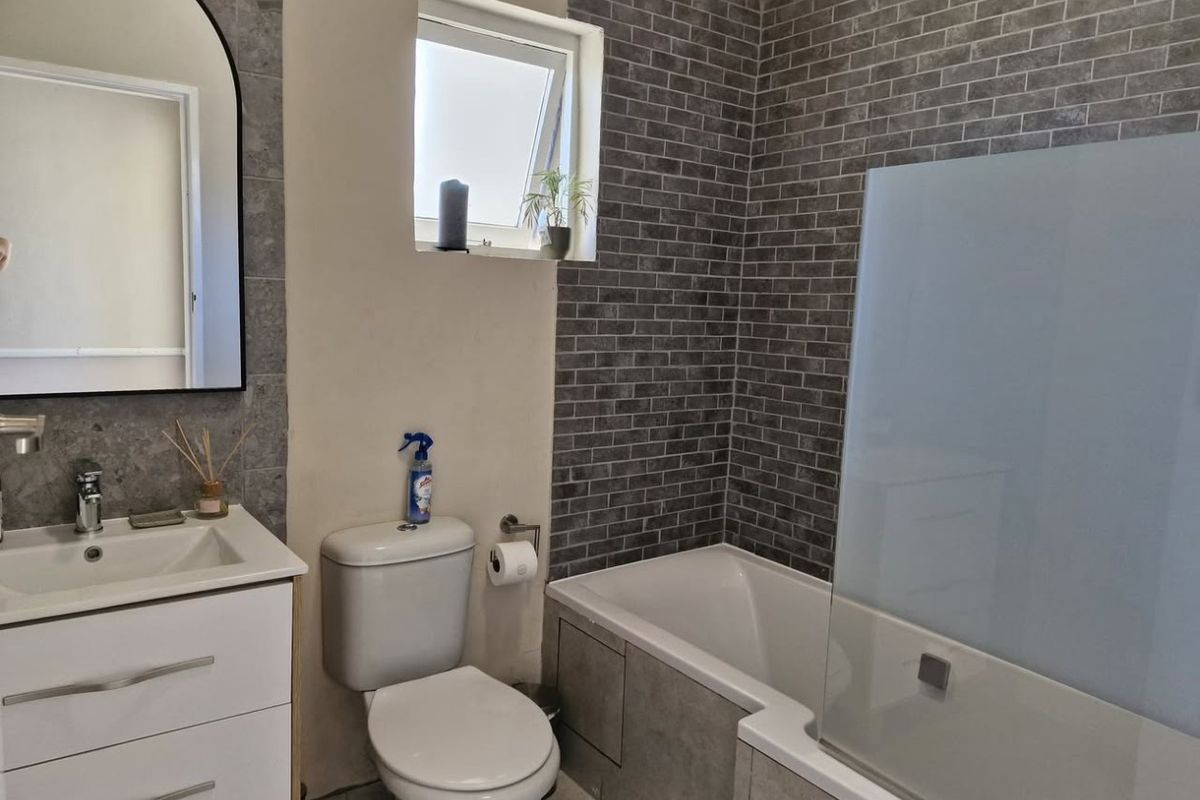 A modern bathroom featuring a vanity unit, toilet, and a bathtub with a glass shower screen, accented by grey brick-style wall tiling.