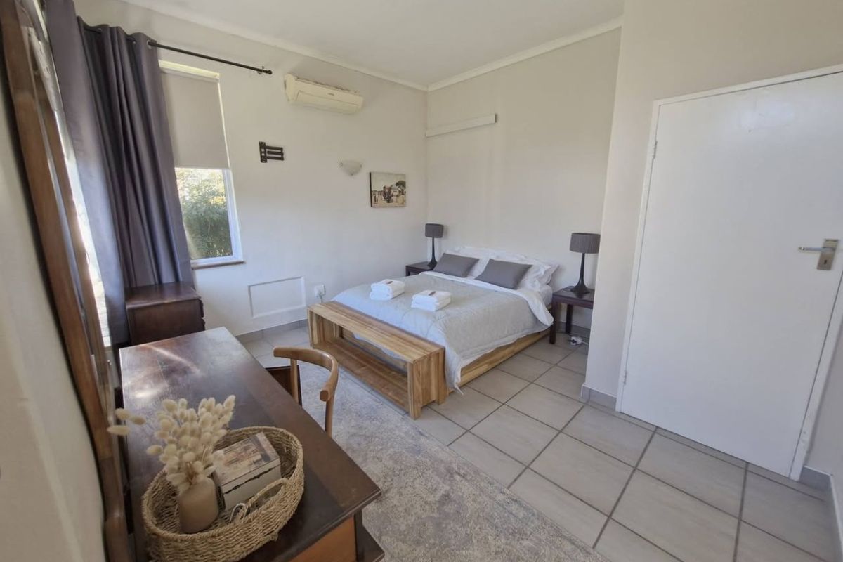 A functional bedroom featuring tiled flooring, a wall-mounted air conditioning unit, and a window providing natural light.