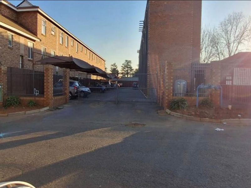 Front exterior view of the townhouse complex featuring a gated entrance, brick facade, and covered parking area.