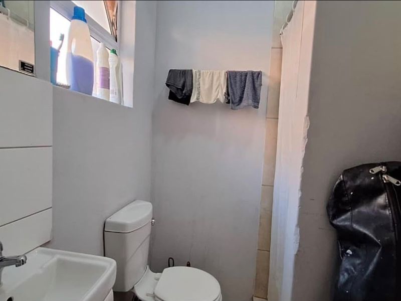 A compact bathroom featuring a standard toilet, washbasin with faucet, and a shower area with a curtain.