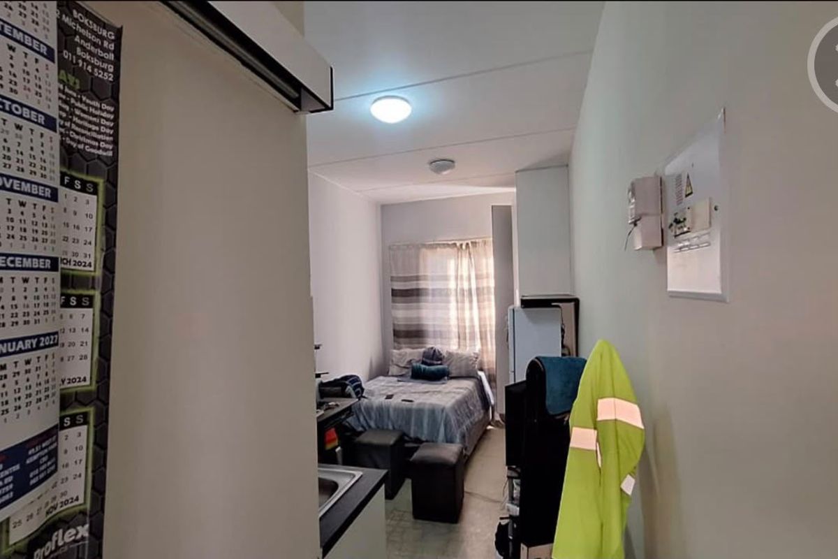 A compact open-plan living and sleeping area featuring a small kitchenette, electrical distribution board, and functional ceiling lighting.