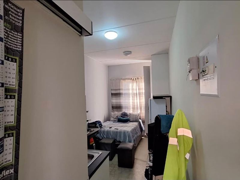 A compact open-plan living and sleeping area featuring a small kitchenette, electrical distribution board, and functional ceiling lighting.