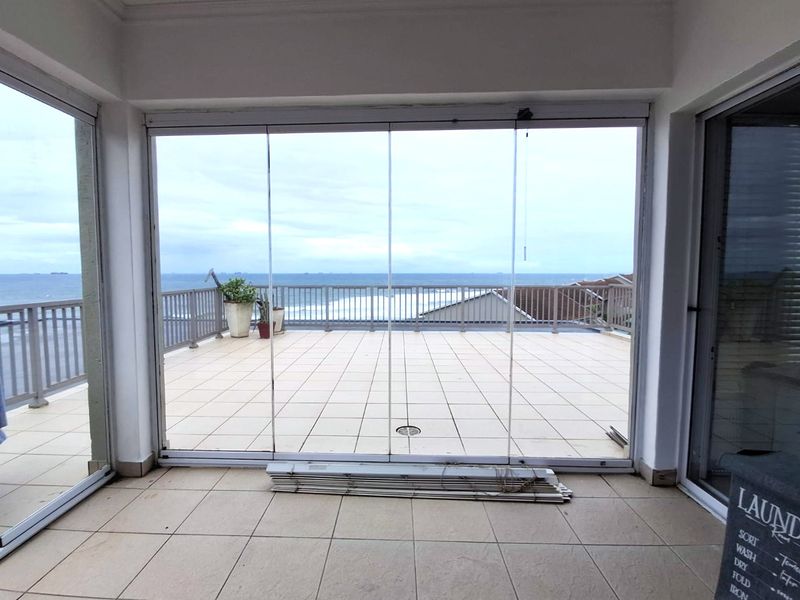 Spacious balcony featuring frameless glass sliding doors, tiled flooring, and a metal balustrade with expansive ocean views.