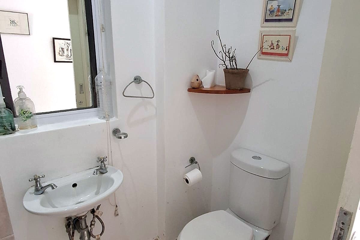 A compact bathroom featuring a wall-mounted basin, dual-flush toilet, and tiled flooring, providing essential utility in a functional layout.