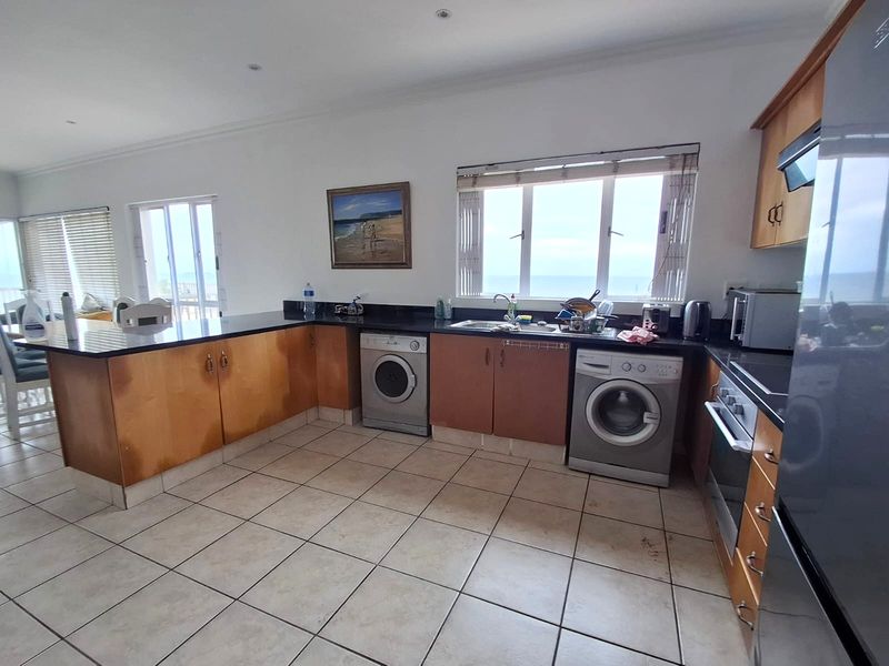 Spacious kitchen featuring granite countertops, built-in cabinetry, integrated laundry appliances, and tiled flooring with views of the ocean.