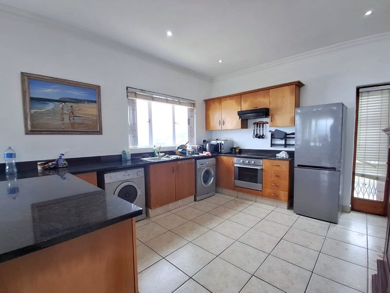 Functional kitchen featuring wooden cabinetry, granite countertops, built-in oven, extractor fan, and tiled flooring with direct access to an outdoor area.
