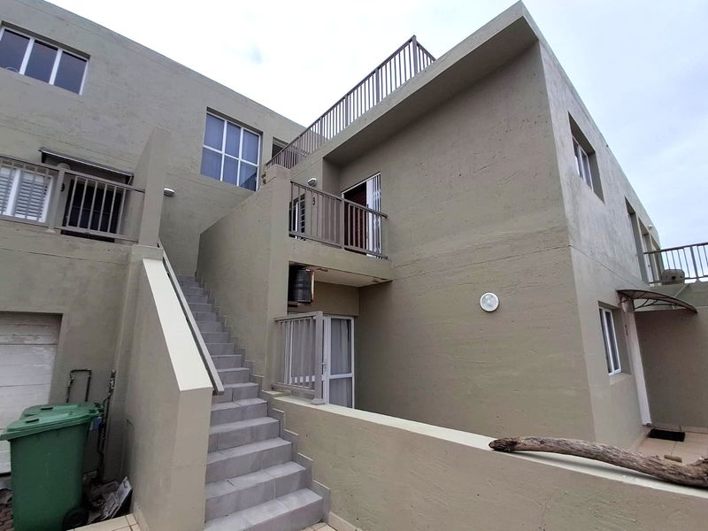 Exterior view of an apartment building featuring a concrete staircase leading to an upper-level balcony with metal railings.