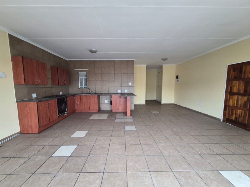 Spacious open-plan kitchen and living area featuring tiled flooring, built-in cabinetry, and a tiled backsplash, offering a functional layout ready for personalization.