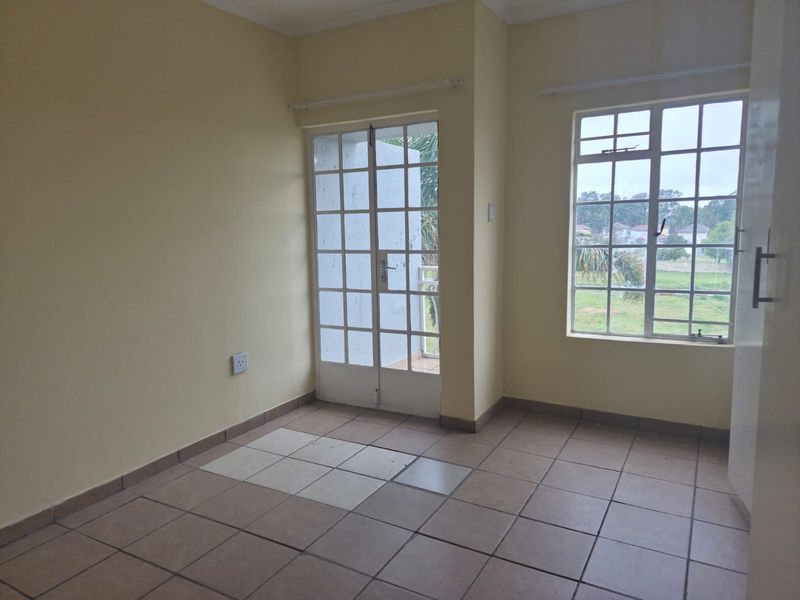 An empty bedroom featuring tiled flooring, a french door leading to a balcony, and a grid window with natural light.