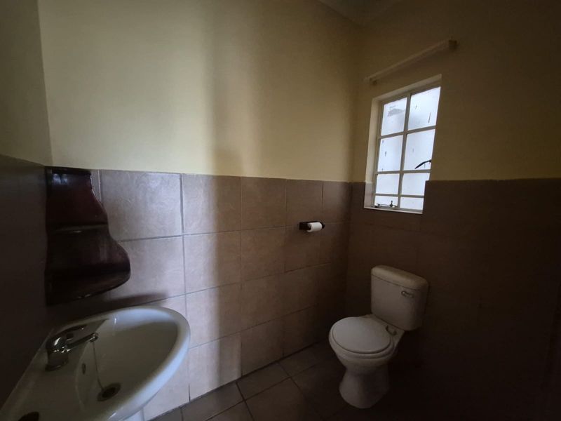 A compact bathroom featuring a pedestal washbasin, toilet, and half-tiled walls. The space is functional but would benefit from cosmetic updates.