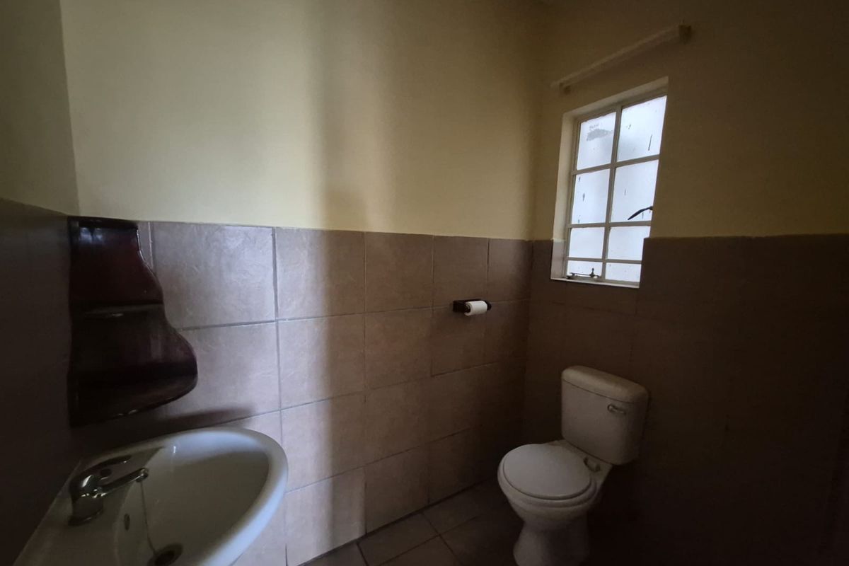 A compact bathroom featuring a pedestal washbasin, toilet, and half-tiled walls. The space is functional but would benefit from cosmetic updates.