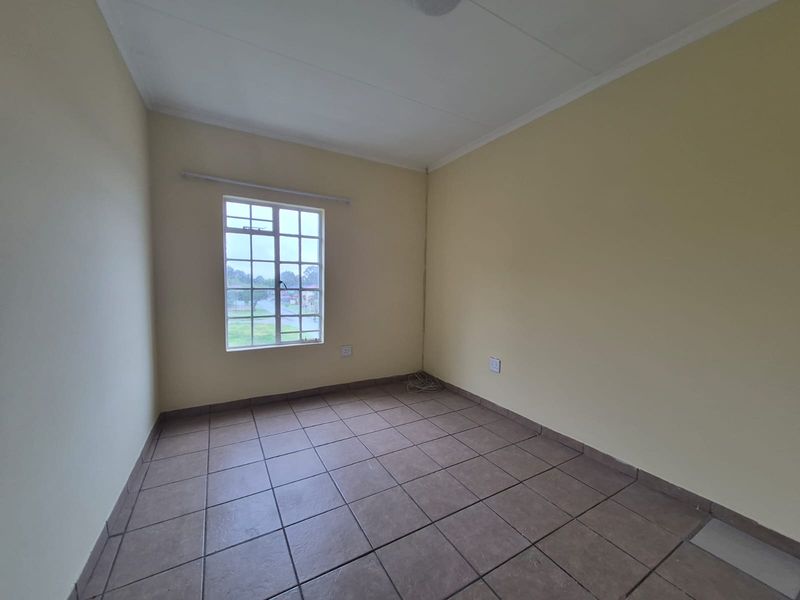 An empty bedroom featuring tiled flooring, neutral walls, and a grid-pattern window providing natural light.