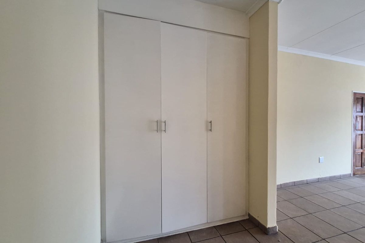 A clean, empty bedroom featuring neutral walls, tiled flooring, and built-in storage cupboards.