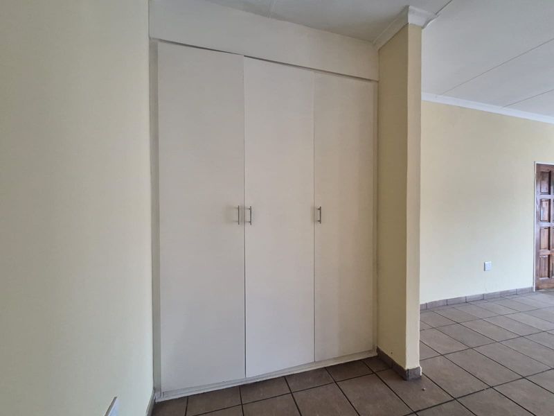 A clean, empty bedroom featuring neutral walls, tiled flooring, and built-in storage cupboards.