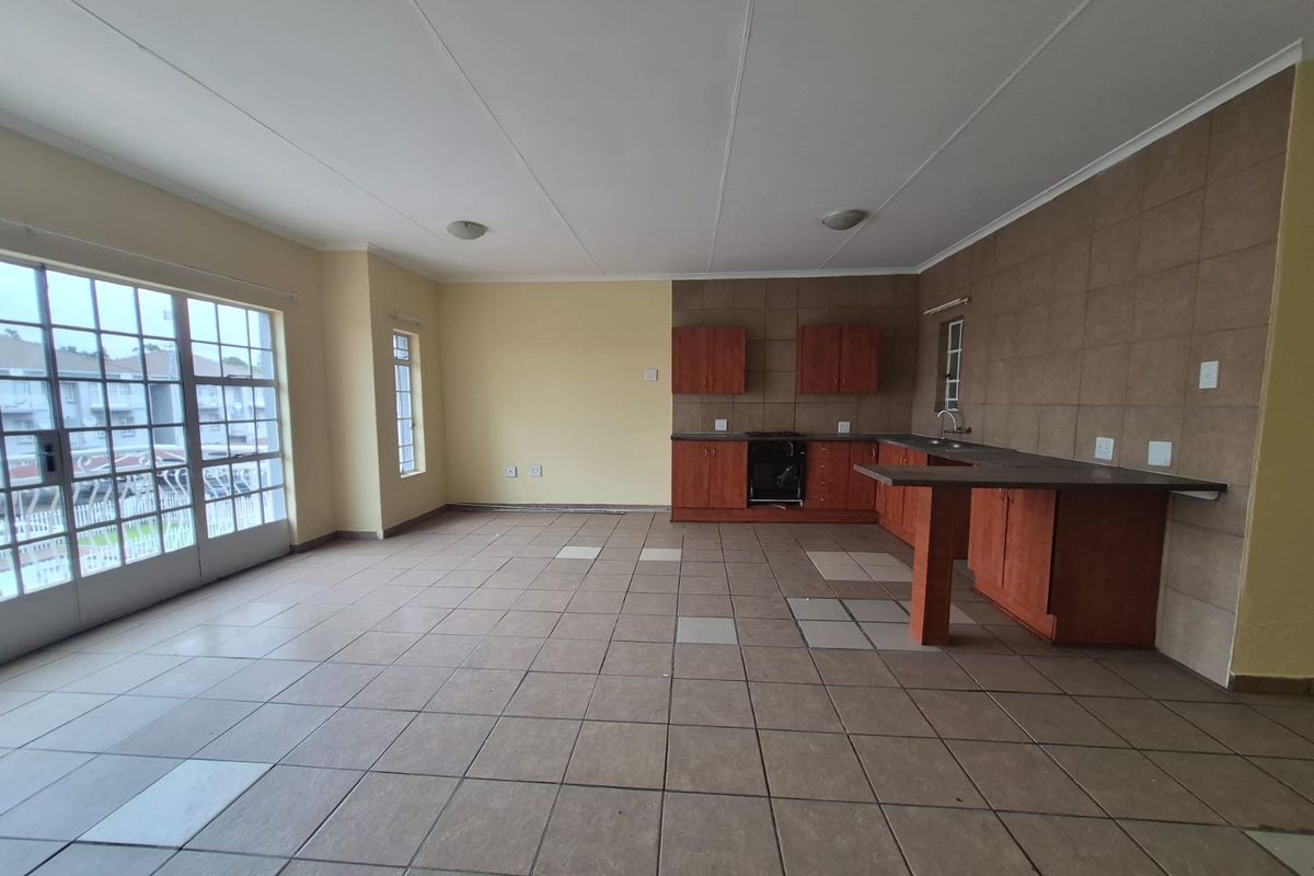 Spacious open-plan living and kitchen area featuring tiled floors, built-in cabinetry, and a breakfast bar, with direct access to a balcony through sliding doors.