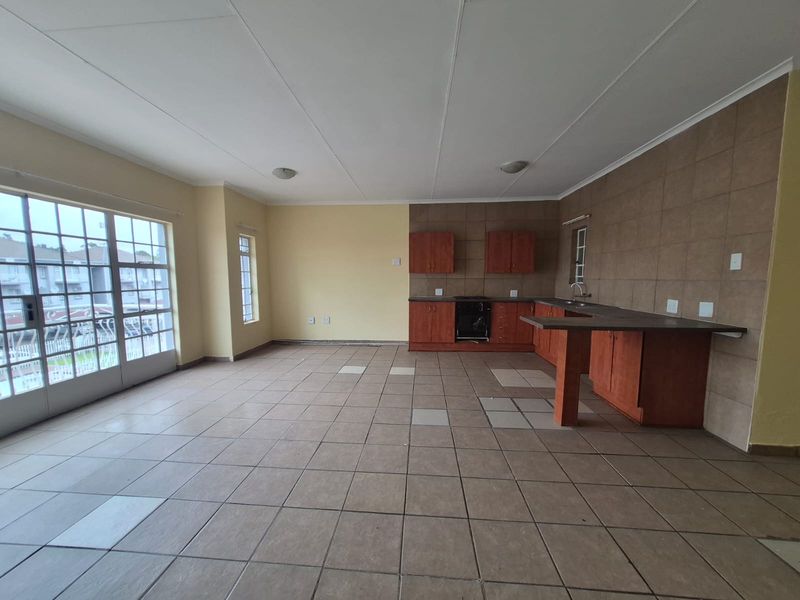 Spacious open-plan living and kitchen area featuring tiled floors, built-in cabinetry, and a breakfast bar, with direct access to a balcony through sliding doors.