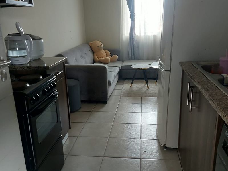 Compact open-plan living area featuring a functional kitchen with granite countertops, built-in cabinetry, and tiled flooring, seamlessly connected to a small lounge space.