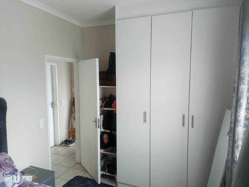 A bedroom featuring white built-in cupboards with modern handles and neutral wall tones, providing ample storage space.
