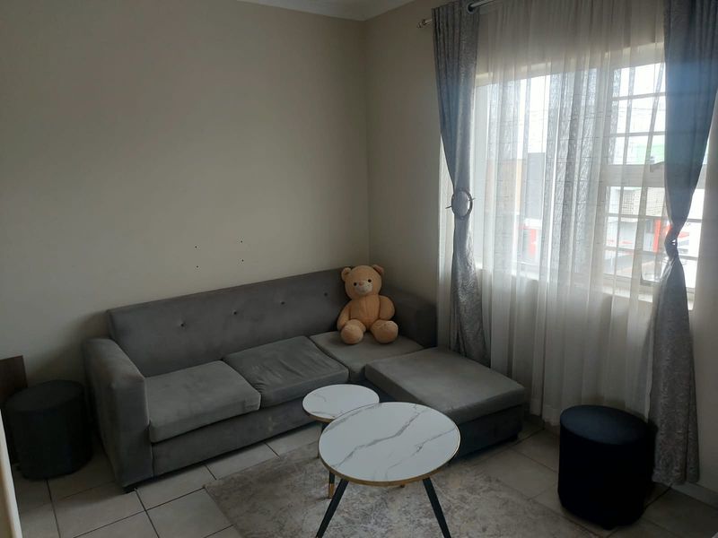 A living room area featuring tiled flooring and a large window with curtain tracks, providing natural light to the space.