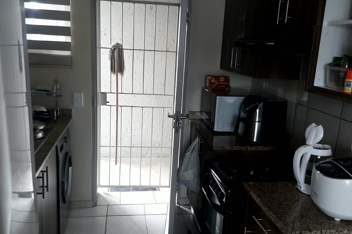 A functional kitchen featuring dark wood cabinetry, granite countertops, tiled flooring, and direct access to an exterior area through a security gate.