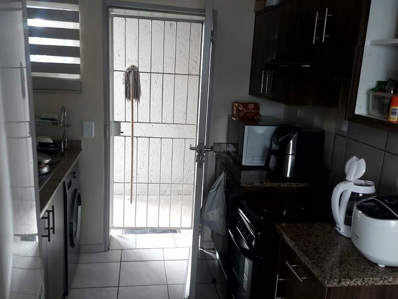 A functional kitchen featuring dark wood cabinetry, granite countertops, tiled flooring, and direct access to an exterior area through a security gate.