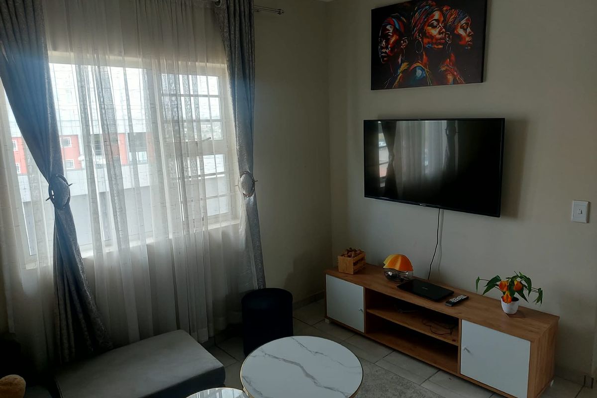 A well-maintained living room featuring tiled flooring and a large window with security bars, providing natural light and a functional layout.
