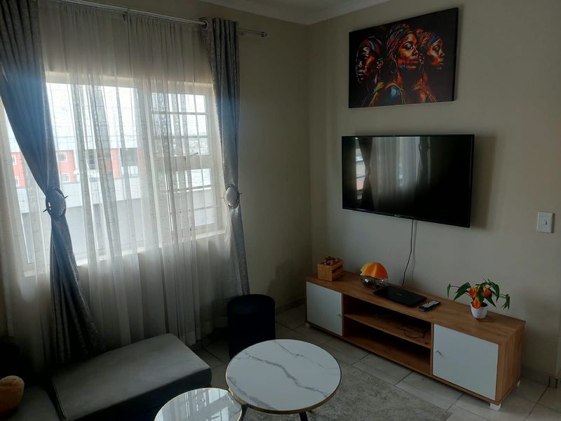 A well-maintained living room featuring tiled flooring and a large window with security bars, providing natural light and a functional layout.