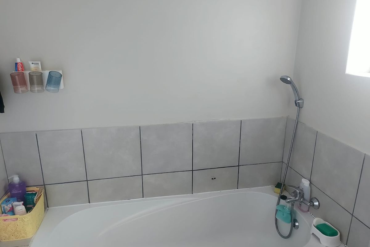 A functional bathroom featuring a bathtub with a handheld shower attachment and neutral wall tiling.