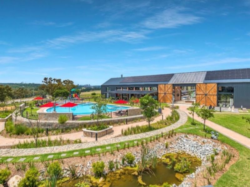 A well-maintained communal pool area featuring stone retaining walls, landscaped gardens, a pond, and a modern building with integrated solar panels.
