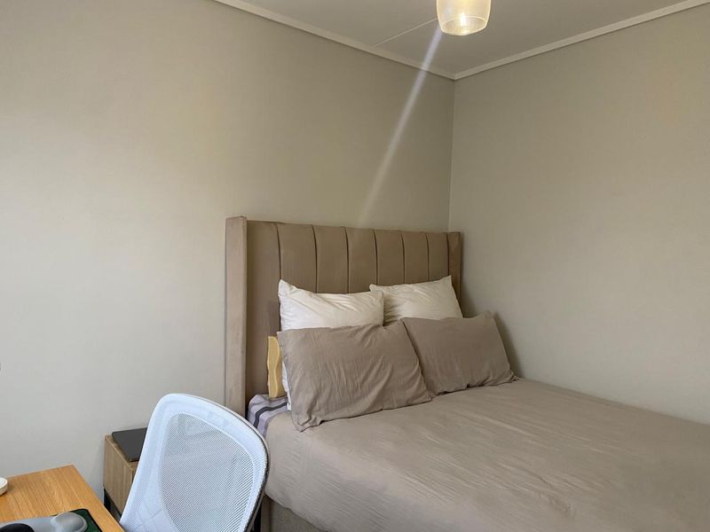 A neutrally decorated bedroom featuring a built-in headboard and simple ceiling lighting, offering a clean and functional space.