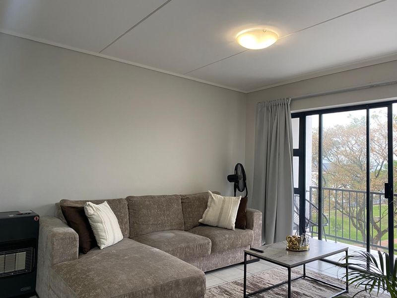 A bright living room featuring tiled flooring and a large sliding glass door providing access to an outdoor balcony area.