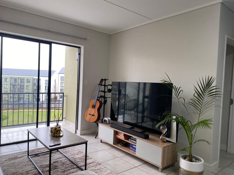 A bright living room featuring tiled flooring and a large sliding glass door providing direct access to a private balcony.